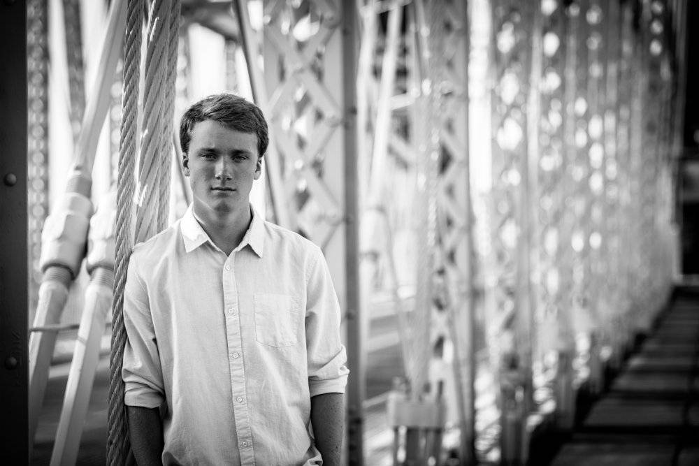 senior boy standing on roebling suspension bridge in cincinnati, black and white unique portrits taken by Krista Nutter Photography