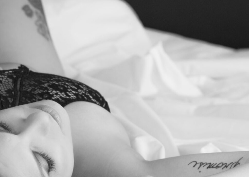 black and white image of woman in black bra with promise tattoo on inner bicep laying on bed upside down beauty and boudoir portraits by Krista Nutter Photography artist vision