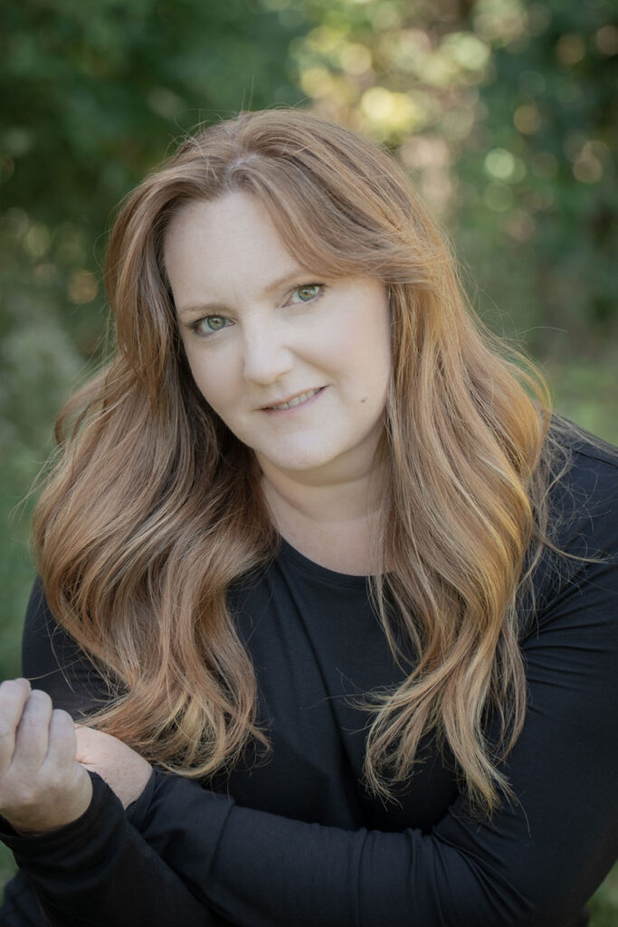 outdoor portrait of Krista Nutter with long red hair and black shirt for about page