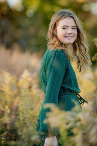 senior girl with blonde hair in a green dress dancing in a field of tall grass at the Cincinnati Nature Center at sunset senior portrait by Krista Nutter Photography Cincinnati
