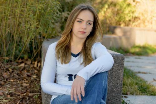senior girl in a white shirt sitting down against a stone wall in a park with fall colors behind her senior portrait by Krista Nutter Photography Cincinnati