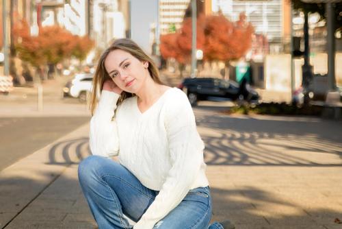 senior girl in a white sweater kneeling down in the street with fall colors behind her senior portrait by Krista Nutter Photography Cincinnati