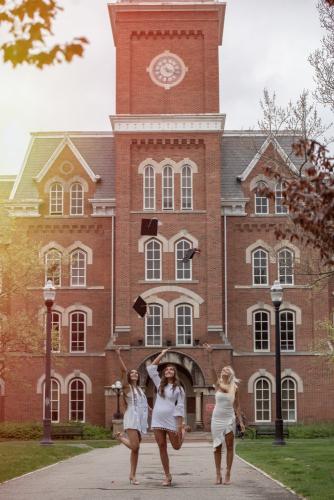three college senior girls throwing their graduation caps in the air in front of University Hall on the Ohio State campus senior portrait by Krista Nutter Photography Cincinnati