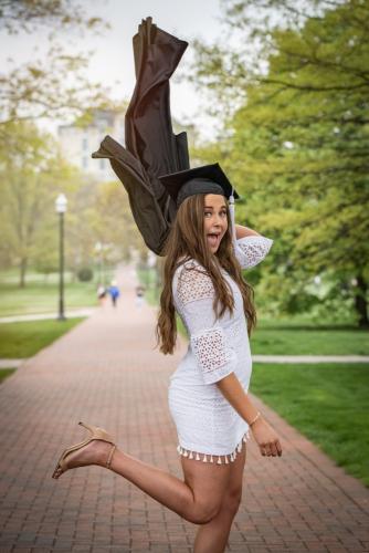 college senior girl in white dress throwing black graduation gown over shoulder making a silly face on Ohio State campus senior portrait by Krista Nutter Photography Cincinnati