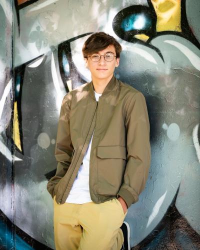 senior boy in brown jacket and white shirt leaning agains a graffiti wall senior portrait by Krista Nutter Photography Cincinnati