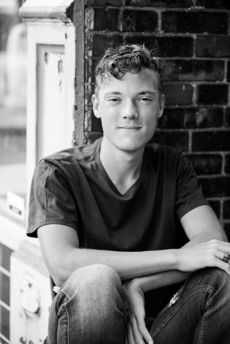 black and white image of a senior boy sitting against a brick wall senior portrait by Krista Nutter Photography Cincinnati