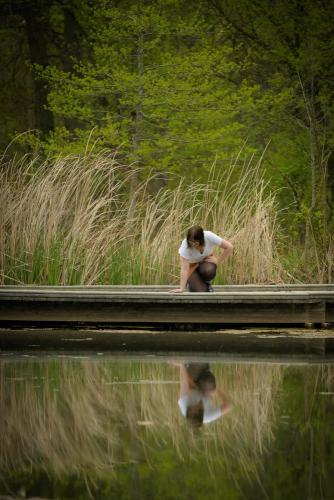 senior girl kneeling down next to water to view reflection and tall grasses behind her at the Cincinnati Nature Center senior portrait by Krista Nutter Photography Cincinnati