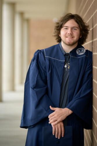 senior boy in blue graduation cap and gown leaning on brick wall senior portrait by Krista Nutter Photography Cincinnati