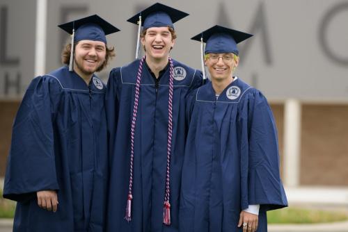 three senior boys in blue graduation caps and gowns smiling in front of a high school senior portrait by Krista Nutter Photography Cincinnati