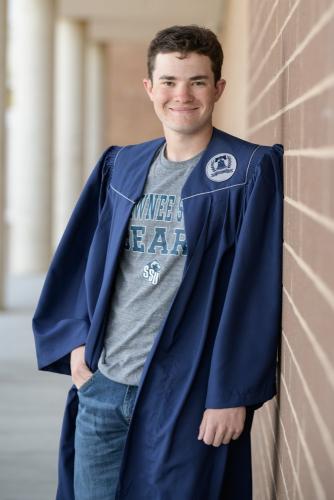 senior boy in blue graduation cap and gown leaning on brick wall senior portrait by Krista Nutter Photography Cincinnati