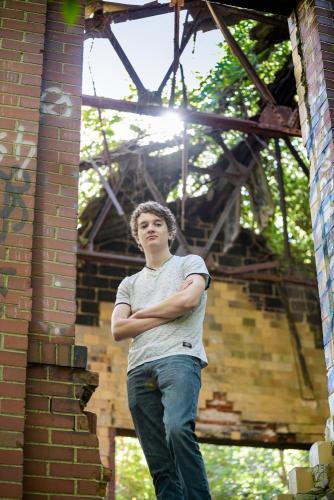 senior boy in an abandoned industrial building standing with arms crossed looking down at camera senior portrait by Krista Nutter Photography Cincinnati