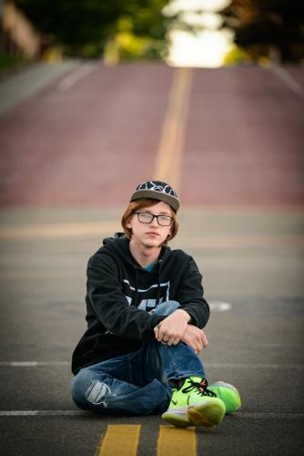 senior boy in hoodie and hip hop baseball hat sitting in middle of brick street senior portrait by Krista Nutter Photography Cincinnati