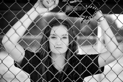 girl softball player looking through the chain link fence in the dugout senior sports portrait by Krista Nutter Photography Cincinnati
