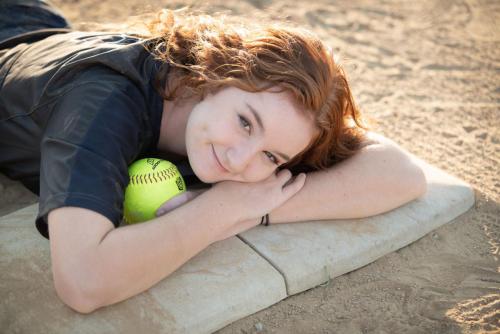 girl softball player laying on a base with a ball smiling senior sports portrait by Krista Nutter Photography Cincinnati