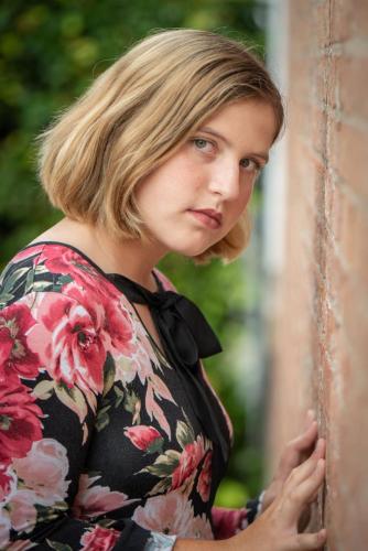 senior girl in floral dress standing leaning against a brick wall senior portrait by Krista Nutter Photography Cincinnati