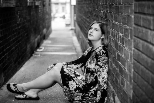 black and white of senior girl in floral dress sitting against a brick wall in an alley senior portrait by Krista Nutter Photography Cincinnati