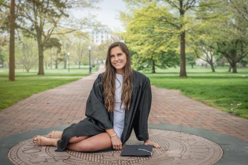 college senior girl in black graduation robe sitting on Ohio State emblem senior portrait by Krista Nutter Photography Cincinnati