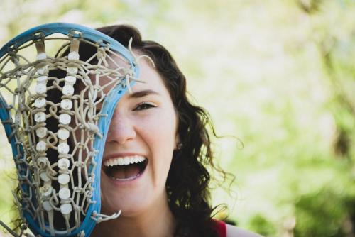 girl lacrosse player laughing looking though the mesh of the stick head senior sports portrait by Krista Nutter Photography Cincinnati