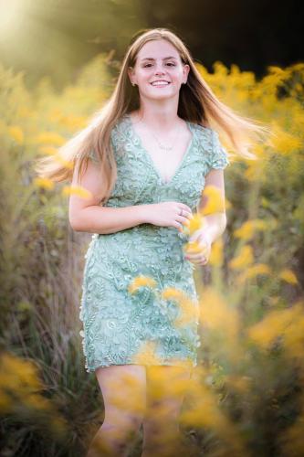 senior girl with brown hair in a light green dress dancing in a field of tall grass at the Cincinnati Nature Center at sunset senior portrait by Krista Nutter Photography Cincinnati