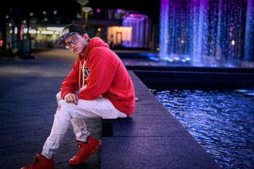 KristaNutterPhotography_2561 senior boy in hip hop outfit on dark street at night near fountain with colored lights headshots and personal branding portraits by Krista Nutter Photography Cincinnati