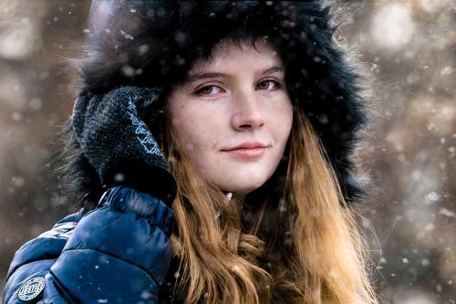 close up of senior girl with blonde hair and a black coat with fur-rimmed hood standing in a snowy field at the Cincinnati Nature Center senior portrait by Krista Nutter Photography Cincinnati